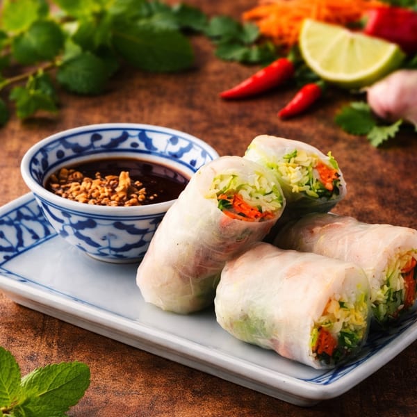 Fresh Thai spring rolls with peanut dipping sauce, chilies, and lime on a brown table.